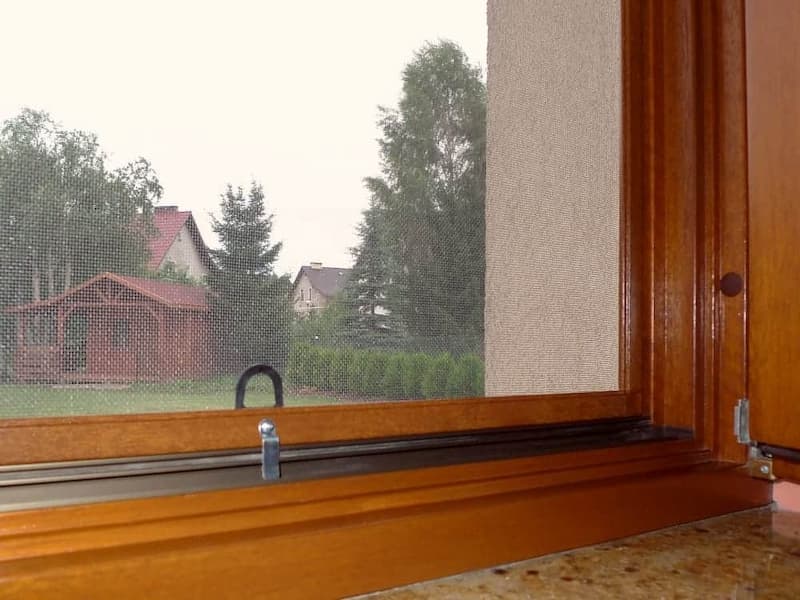 Moskitiera w drewnianym oknie z widokiem na ogród — siatka niemal niewidoczna z wnętrza